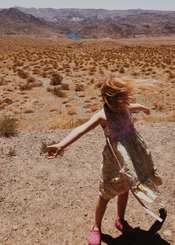 Photo using the Rule of Thirds that shows motion. The photo is of a little girl with her arms out as the wind blows through her hair and dress in front of a desert background. 