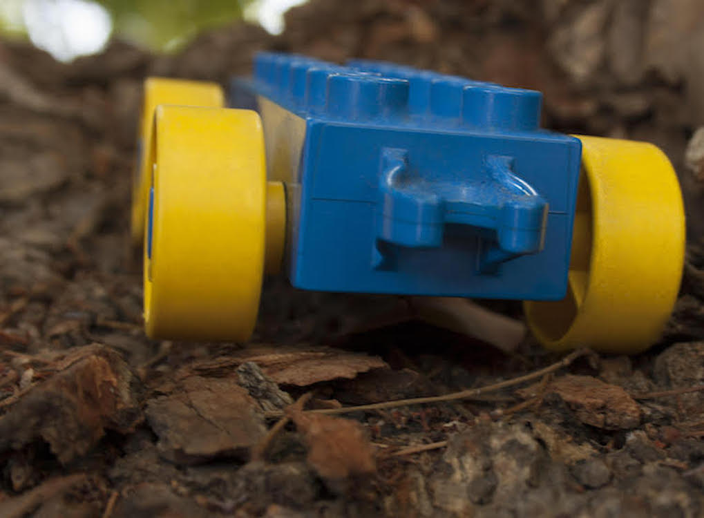 This is a photo of a blue yellow lego car with bright yellow wheels on tree bark.