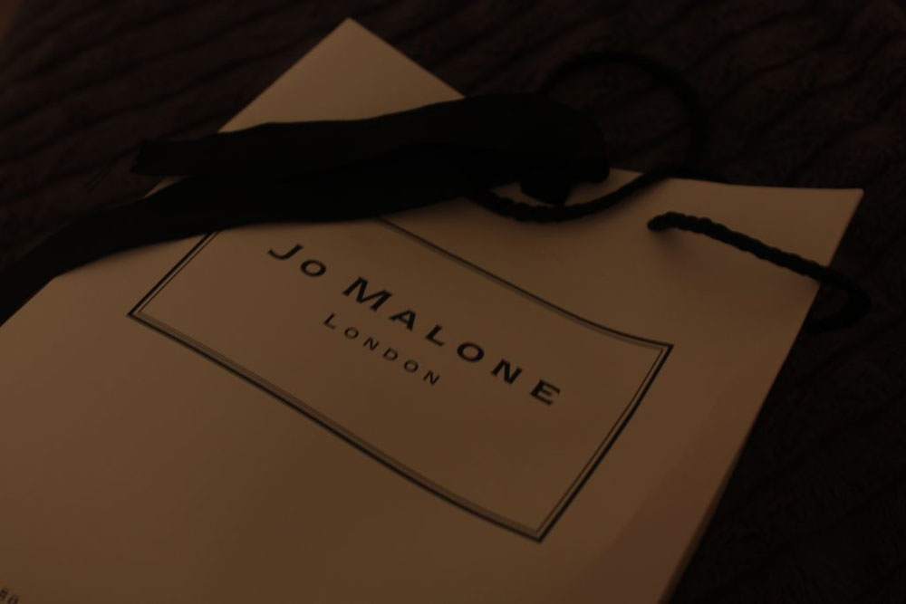 Background is black and main focus is a white and black Jo Malone bag with a ribbon across it