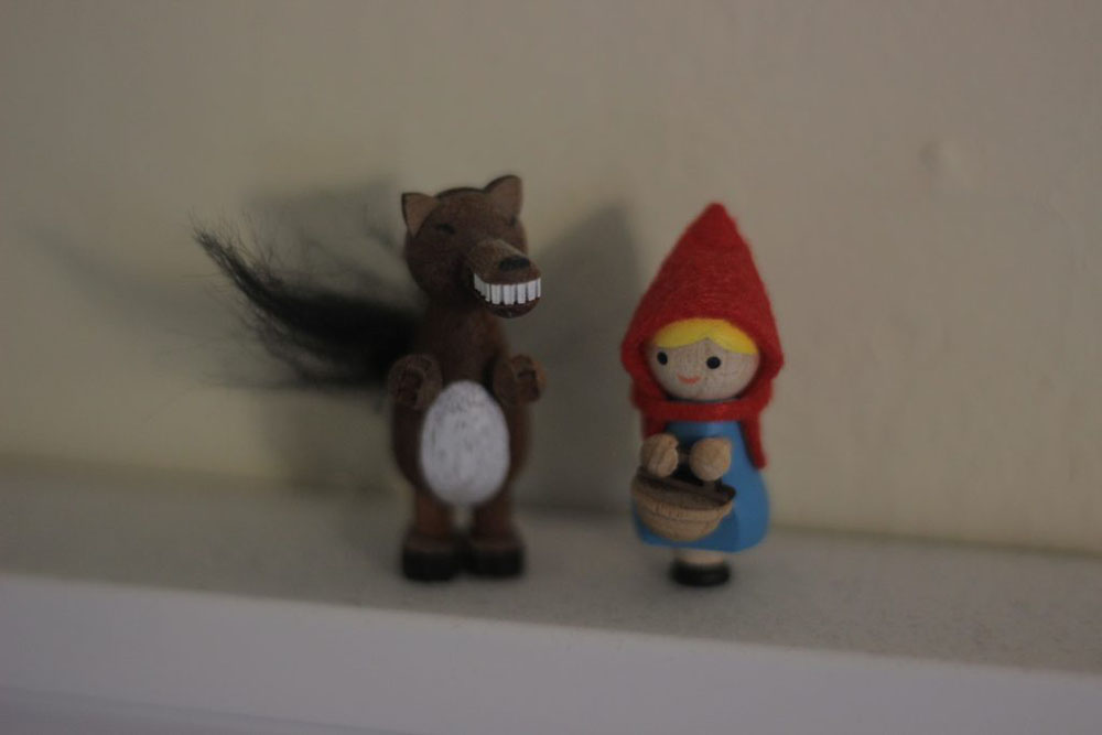 two small wooden figurines: A wolf with a bushy tail, and little red riding hood with a basket. 