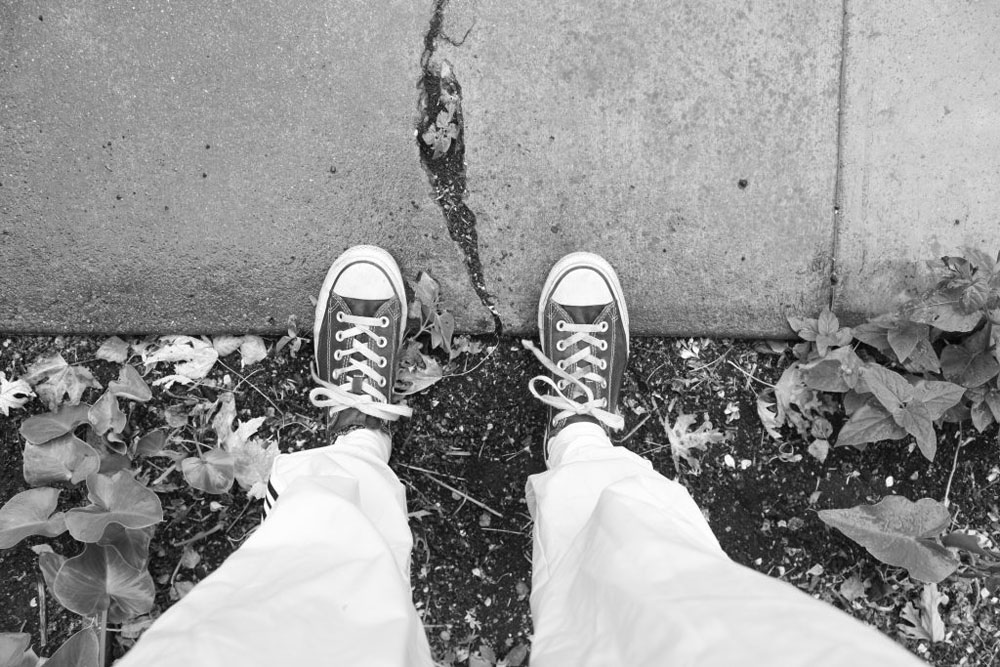 Black and white photo of shoes in dirt and on sidewalk with crack