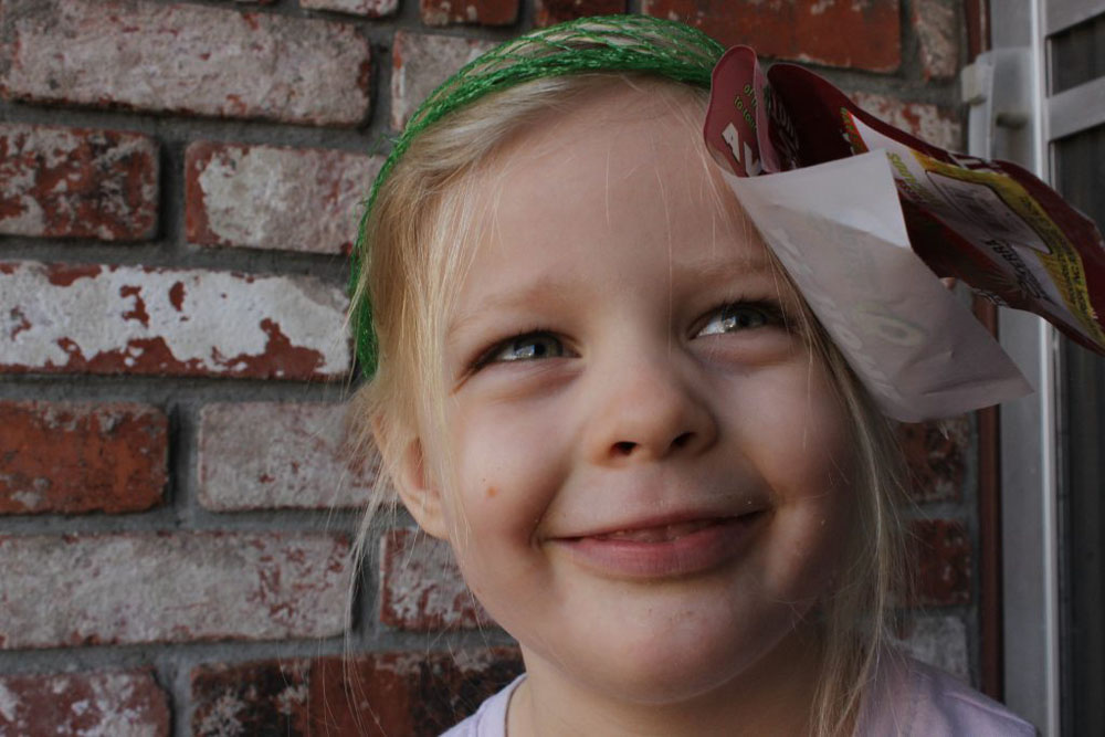 Small girl with avocado net on her head, like a hair net.