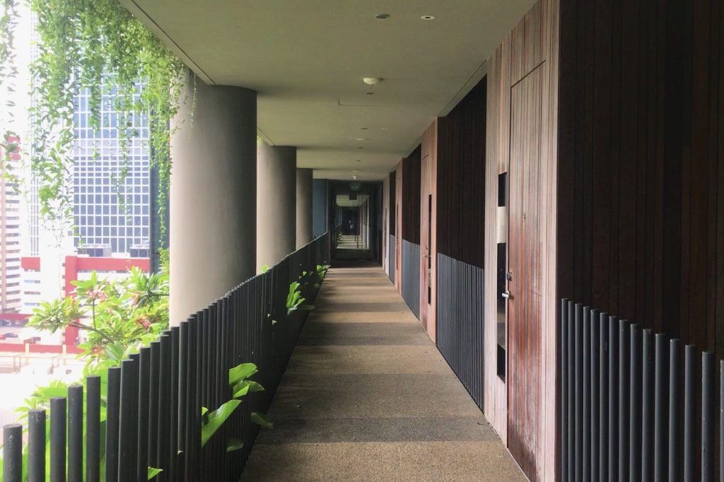 A photo of a hallway in a hotel in Singapore. On the right there are doors to rooms and on the left there is a view of the city. The left and right sides form lines that make the hall seem endless.