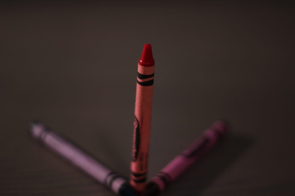 Three crayons in a symmetrical pattern. The center crayon is red and is positioned upwards.