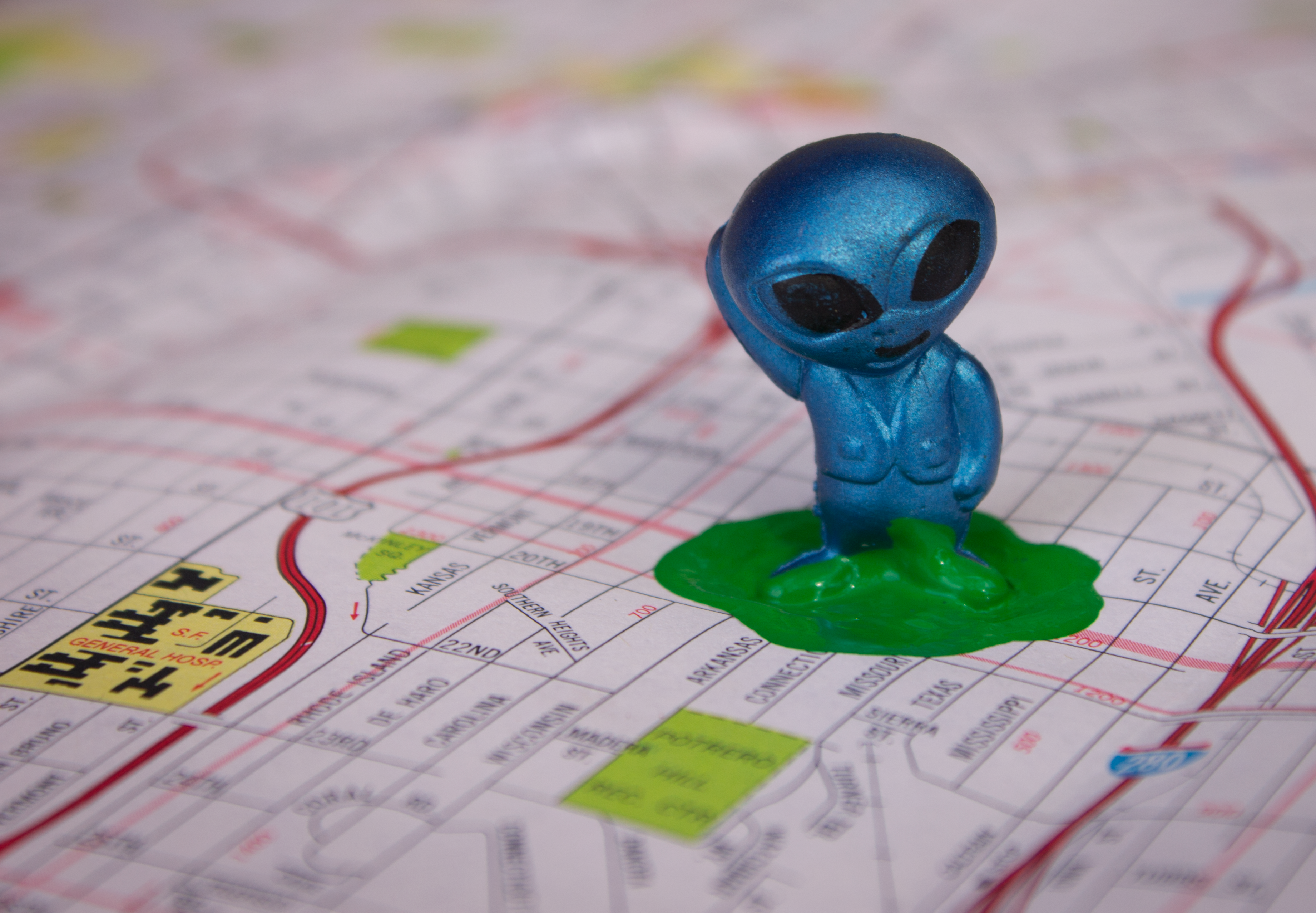 The photo is of a toy alien standing in a puddle of green paint on a map.