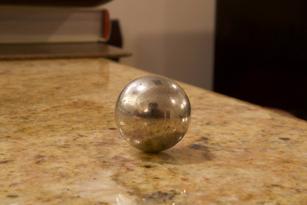 Centered in the image is a metal ball, similar to a marble. It rests on a brown marbled-stone surface. 