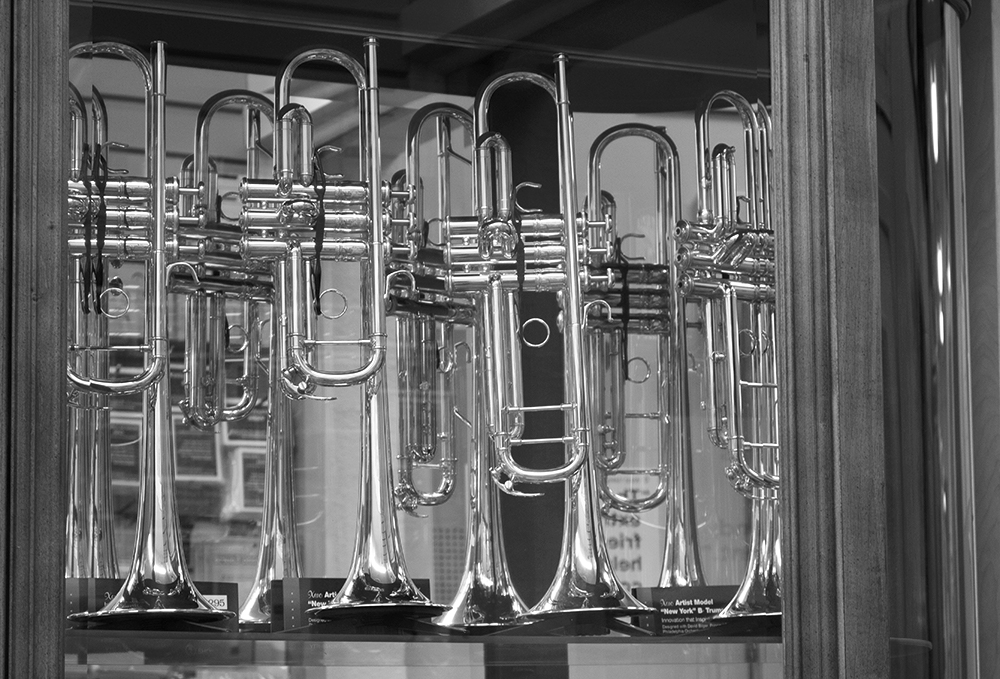 A number of trumpets, balanced on the horn, are encased in a glass case. The picture is in black and white.