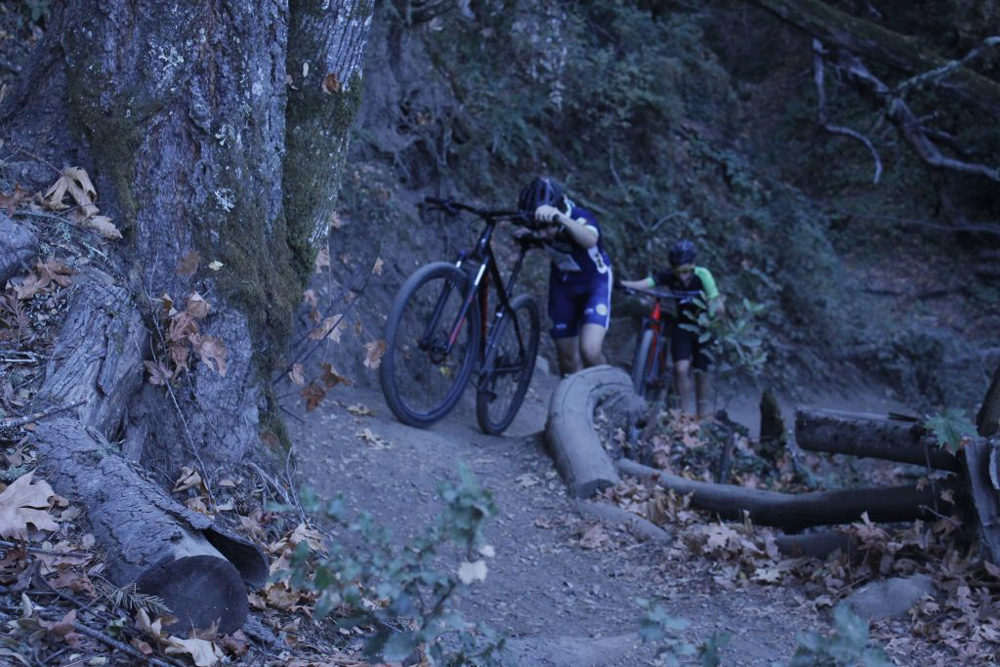 This is a picture of 2 people walking their bikes up a loose and steep trail.