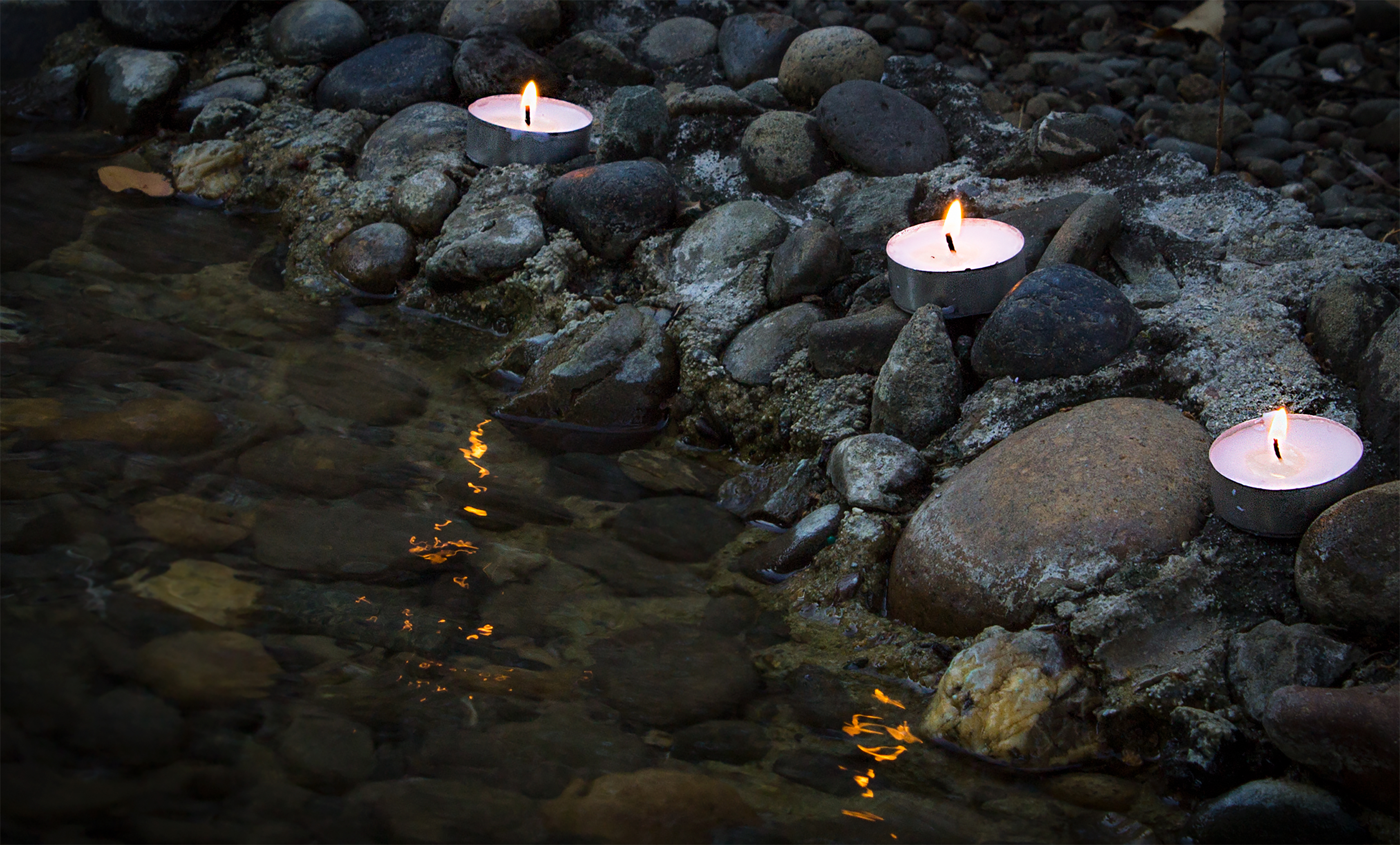 This is a picture of candles on rocks beside a stream.