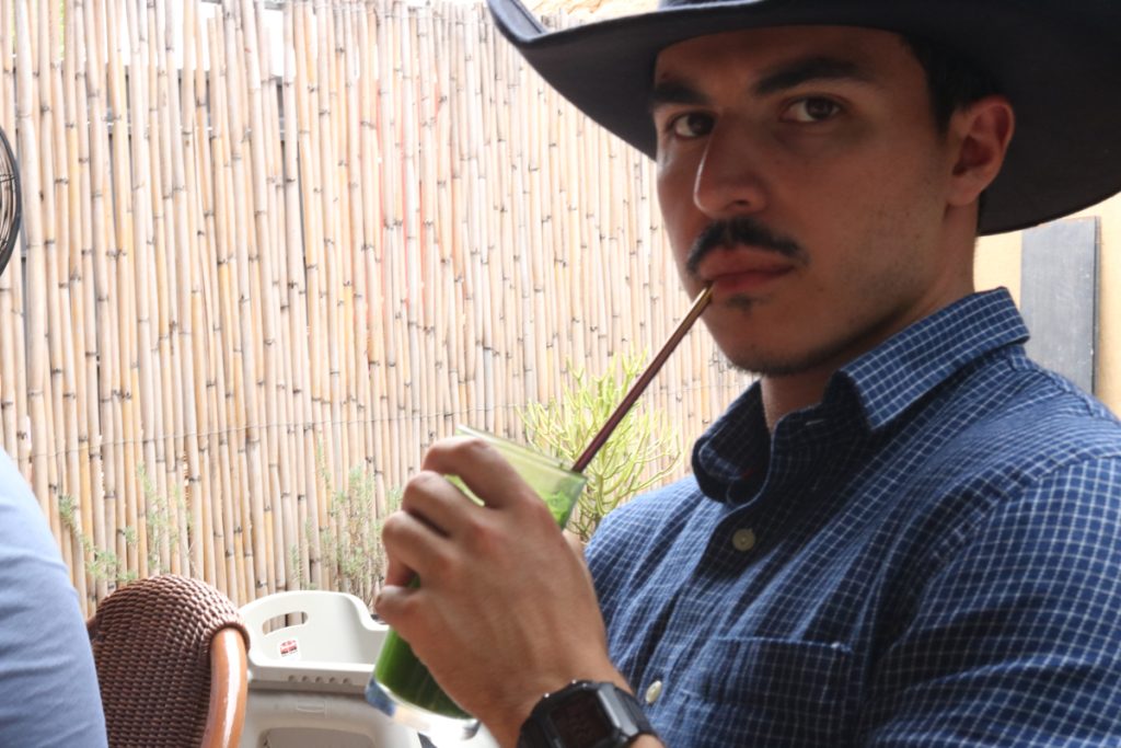 A really cool guy with a black sombrero and blue shirt drinking a drink