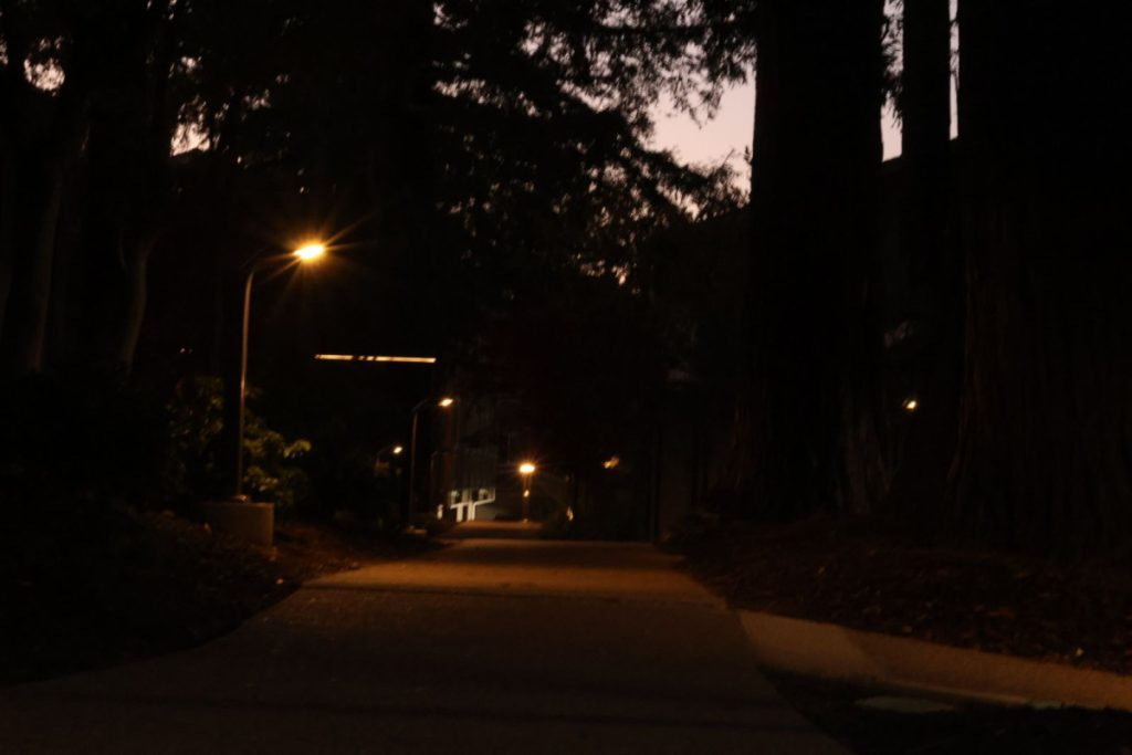 a path that is iluminated by orange lights with a sunset in the background.