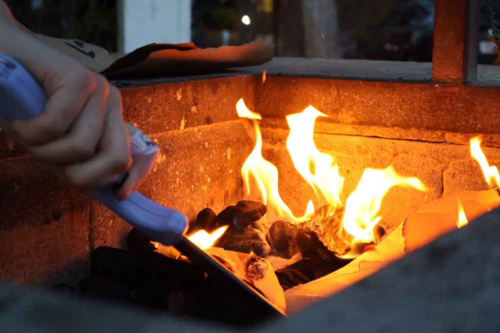 someone with a lighter setting light to a fire in a grill