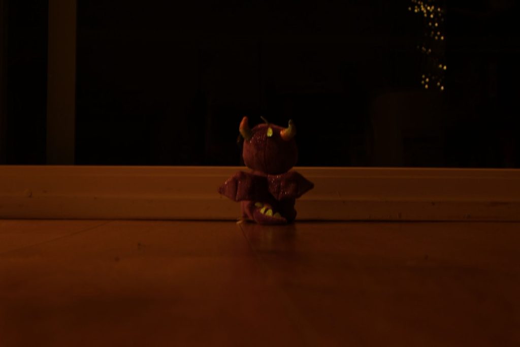 a dragon plush looking outside a balcony window while it is pitch dark.