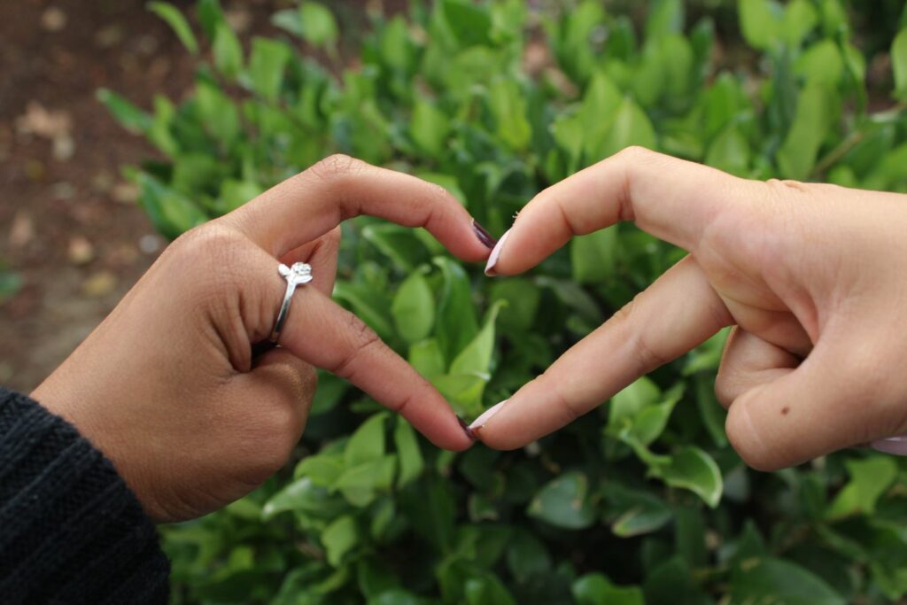 finger heart over a green bush