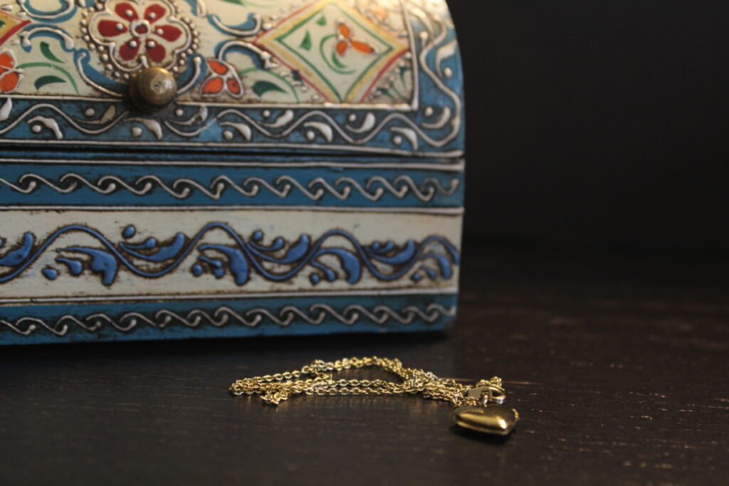wooden jewelry box with a gold heart pendant lying on the table in front of it