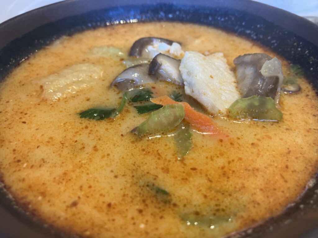 a bowl of galangal soup with coconut milk, chicken, mushrooms, carrots, and celery
