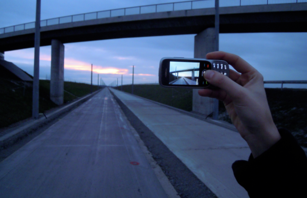 A person's hand holding a camera, taking a picture of a road.