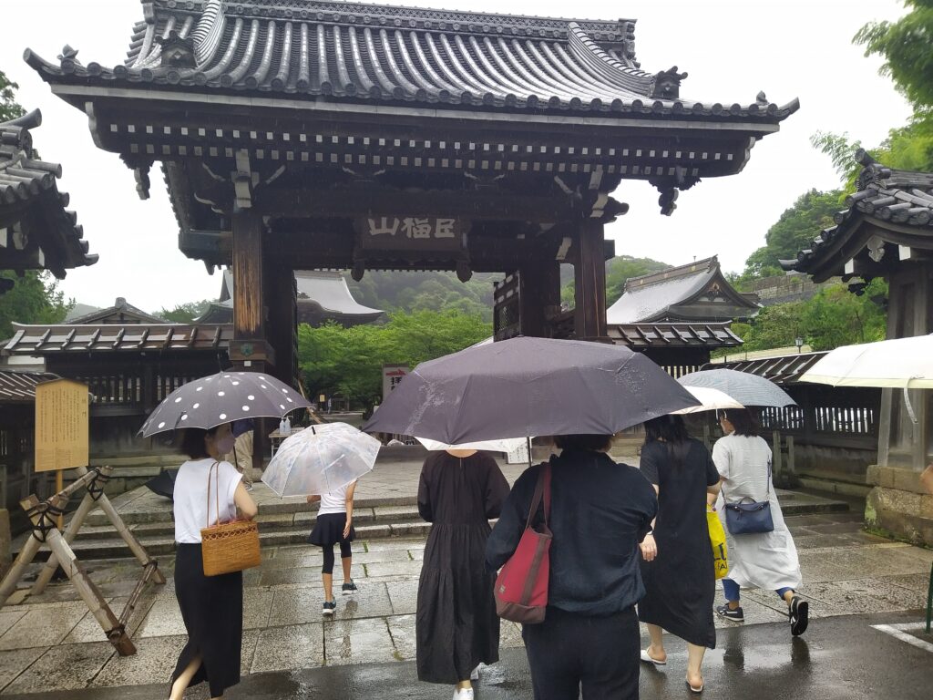A group of people walking into a temple courtyard, as it is raining. 