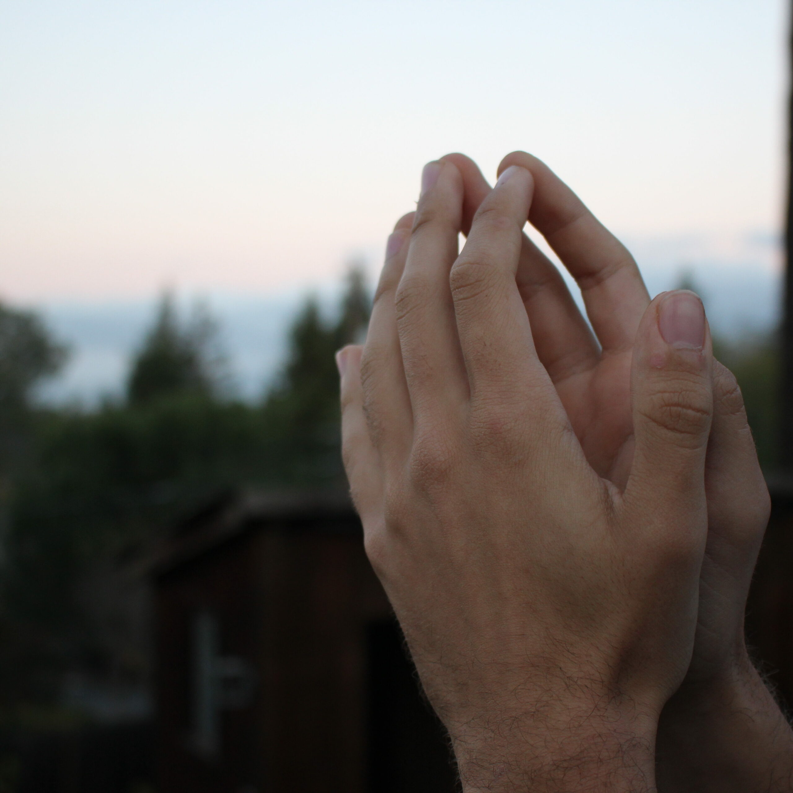 Hand in prayer position in front of the sky