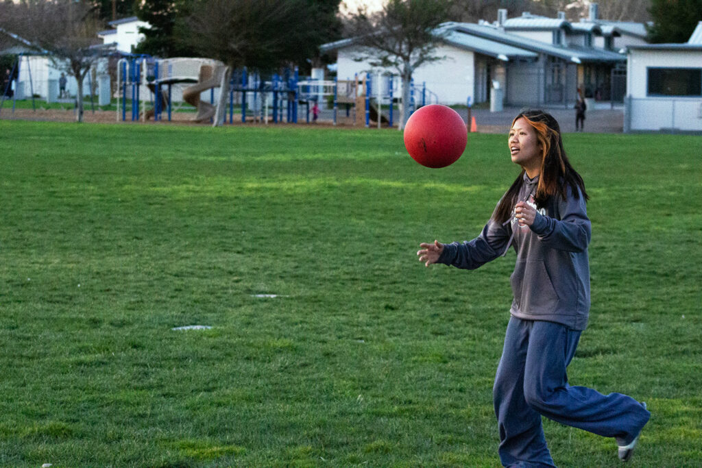 A girl playing with a red ball with a playground behind her
