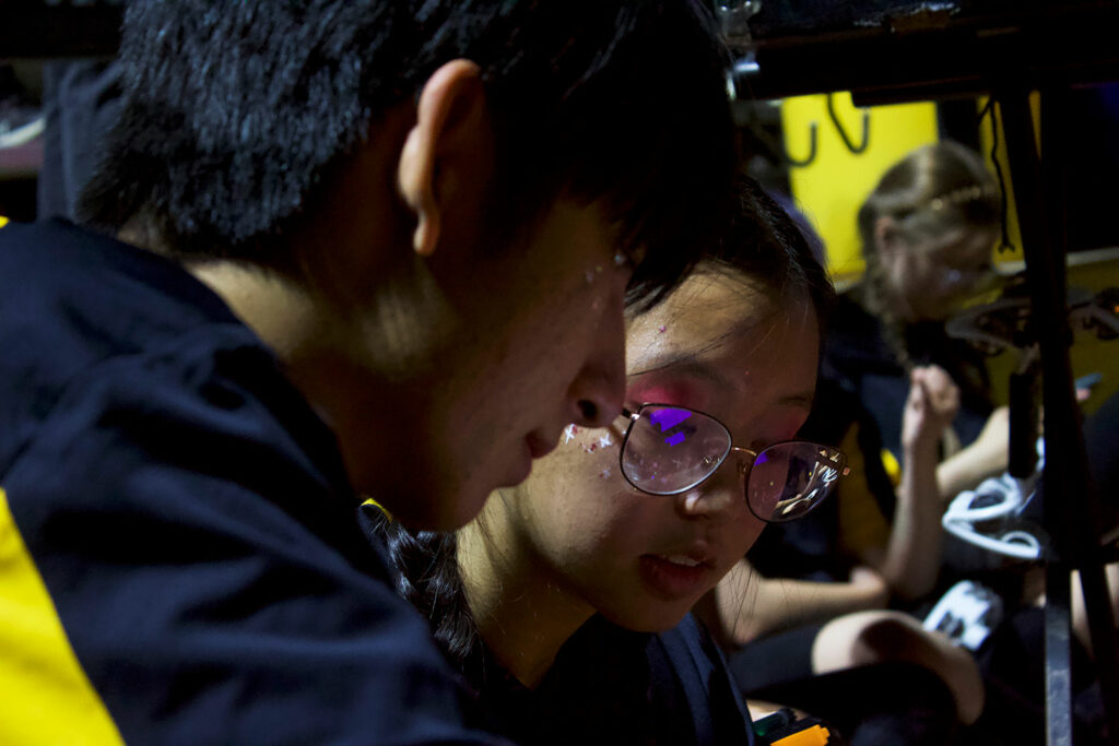 A close up of a boy and a girl, both of them looking downwards at a computer during a football game
