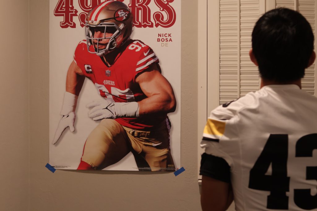 Photo of teen in a white 43 jersey looking at a Nick Bosa Poster