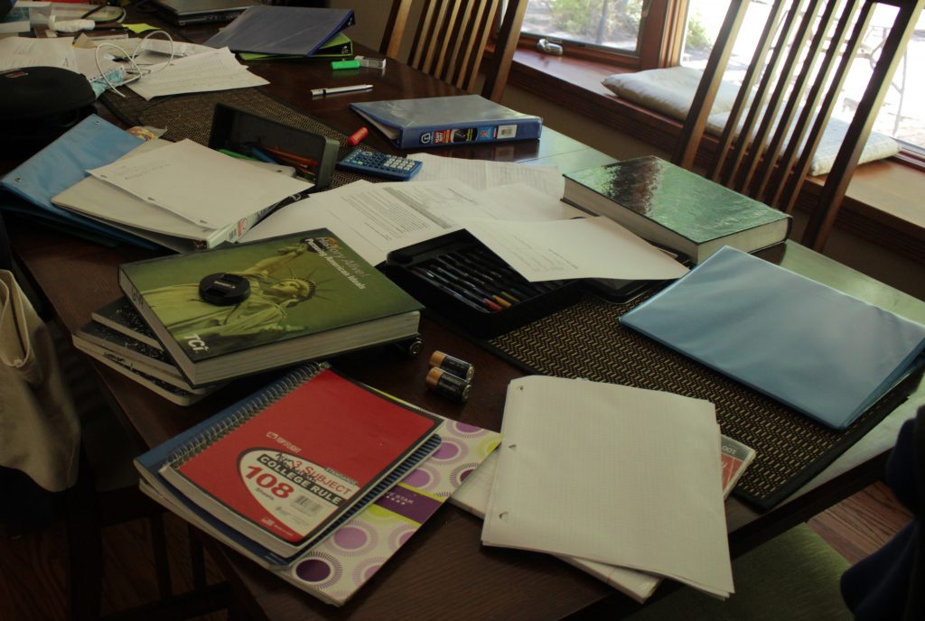 This photo shows a very messy table with binders, textbooks, pencils, notebooks, etc. scattered around.