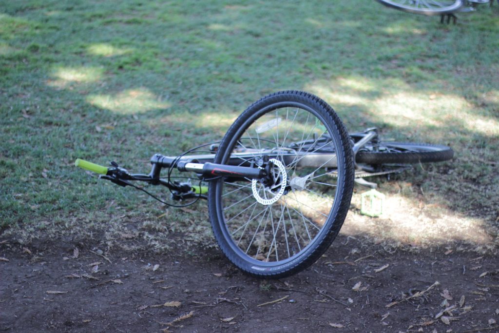 This image shows a bike that is laying on the dirt ground, but one of its wheels is somewhat vertical.