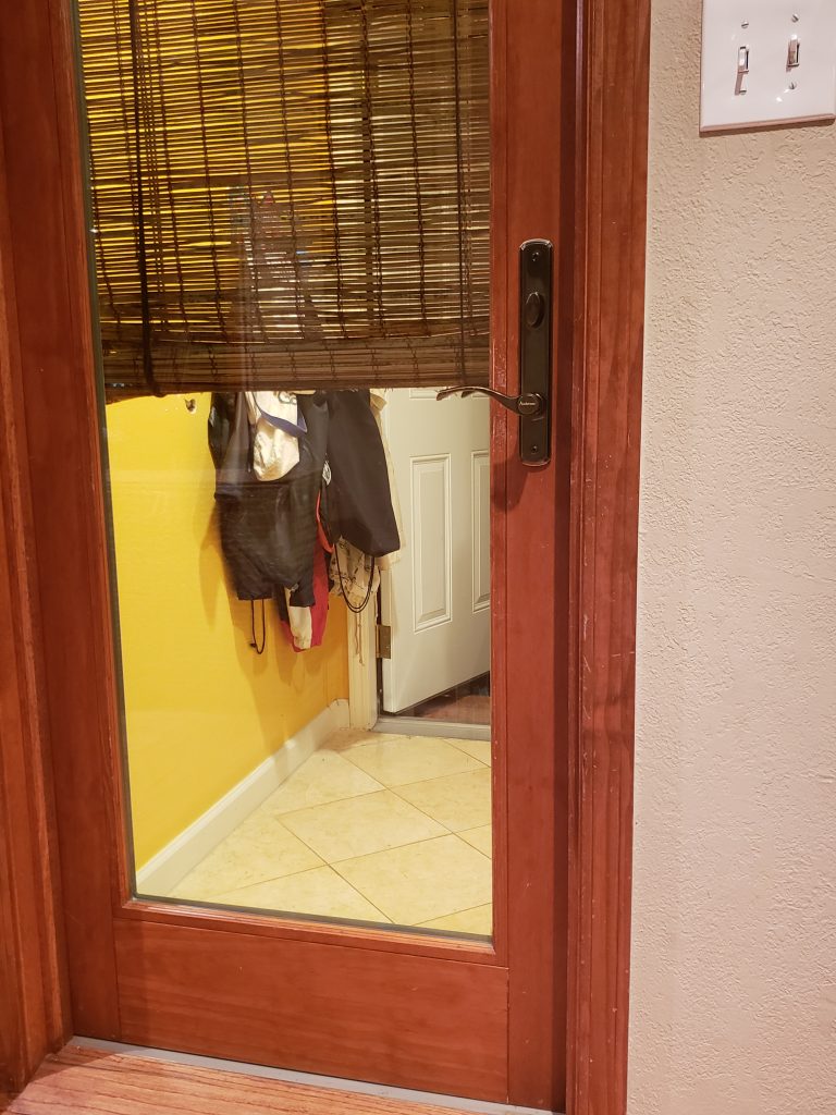 This photo shows a glass and wood door leading into a tiled room with another white door behind it. We can't see what is behind the white door.