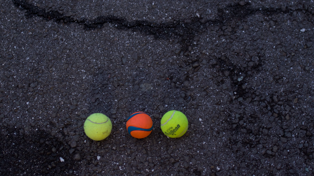 This photo shows three balls. In the middle, there is a dog ball and there are two tennis balls to the left and right of the center ball. The balls are all against a dark background.