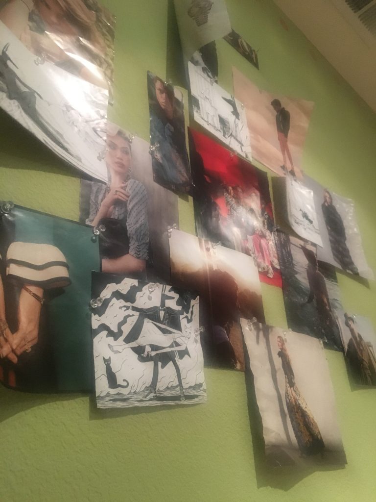 A shot looking up at a variety of magazine advertisements and photos that have been ripped out and pinned onto a green wall.