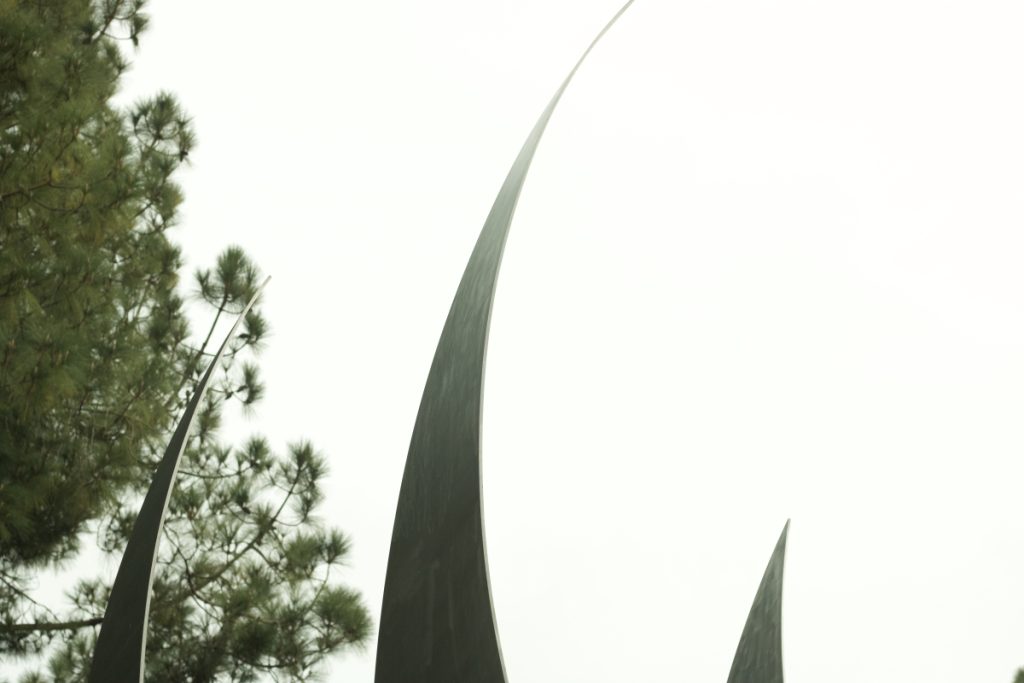 Three silver spikes, one reaching up to the top of the photo, with a tree on the left side.