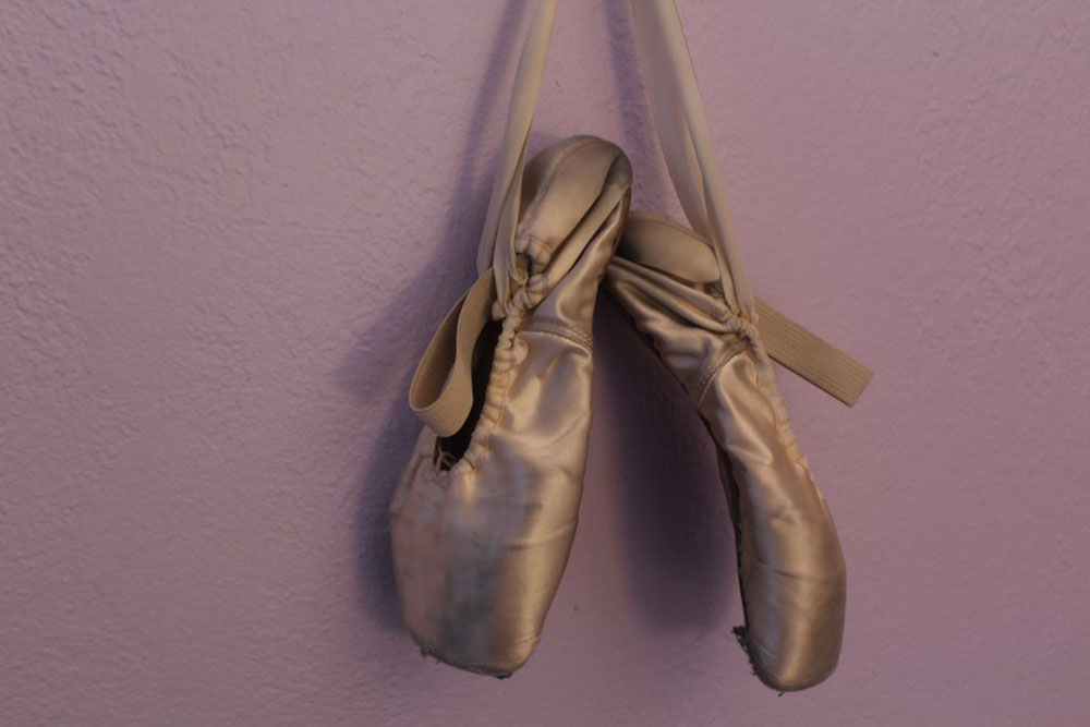 This is a photo of dirty pink pointe shoes against a purple wall. 