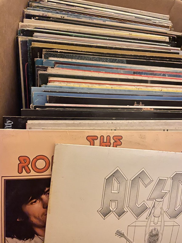 A line of old records stored in a cardboard box. The corner of a white ACDC record and a light orange Rolling Stones record is visible. 
