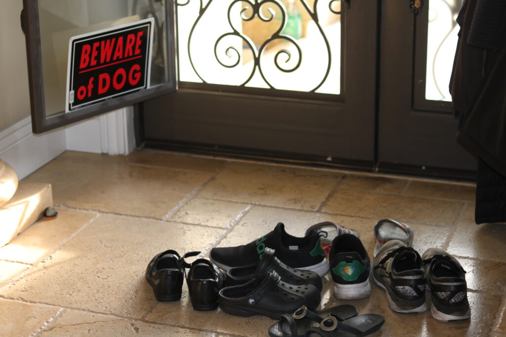pairs of shoes piled and a beware of dog sign being hung in front of the door.