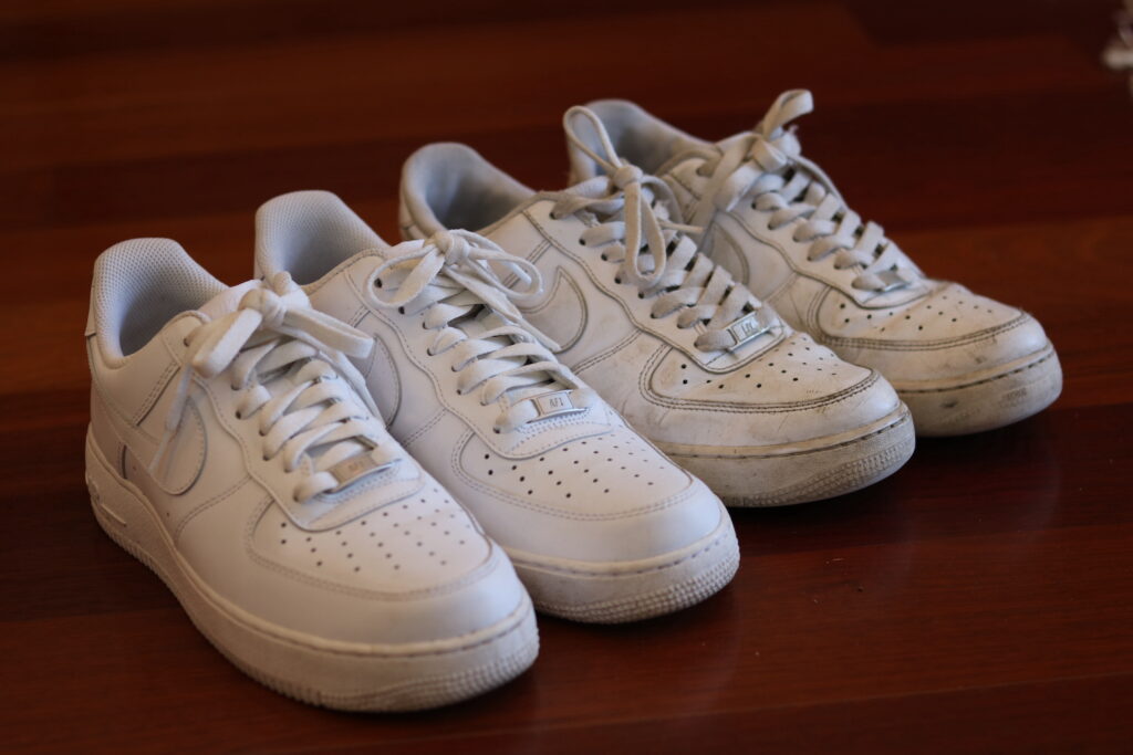 2 white pairs of shoes pair on left is new pair on right is old and smaller