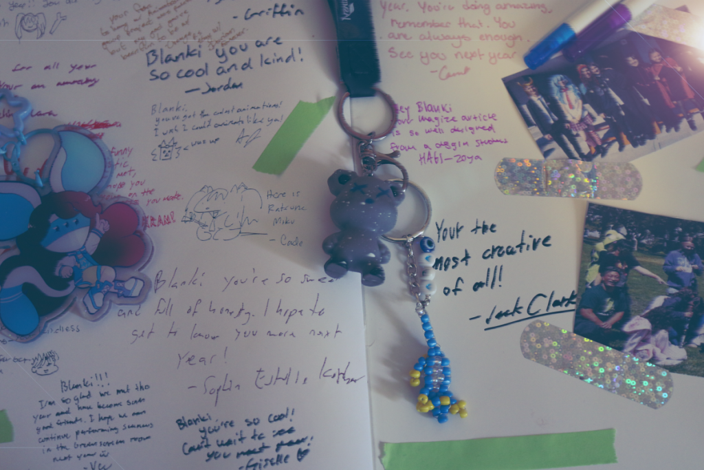 A photograph of last years Freestyle Yearbook with various signatures from my classmates. Additionally, there are two photos taped in, one being from the SFMOMA trip and the other being from Halloween 2025. There is additionally two keychains. One is of my OC, Eon, and the other is from my backpack along with a lizard charm gift from my friend Vee. Taken at F/4, 1/49 Shutter Speed, 1000 ISO, 55mm Lens.