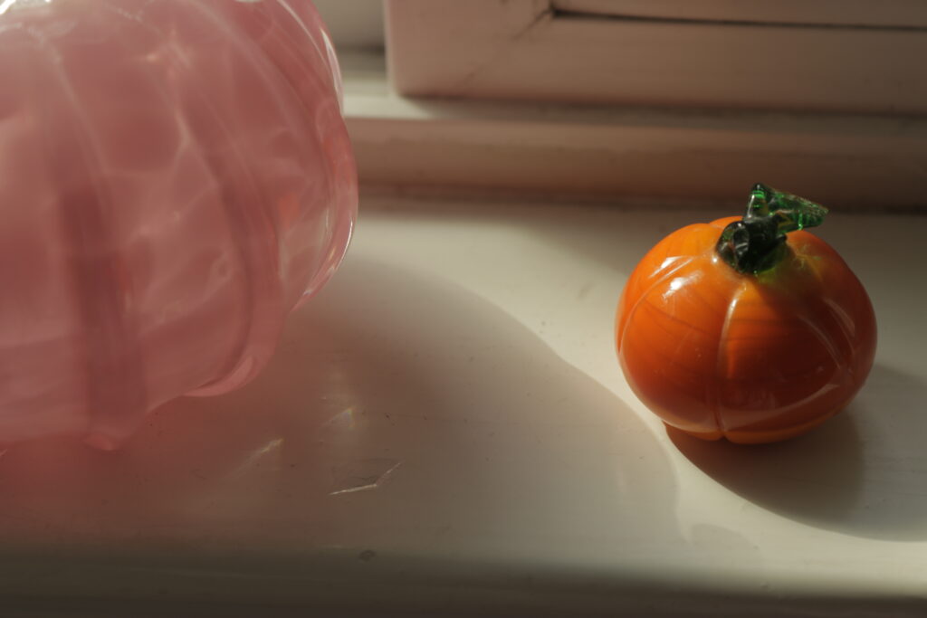 light pink glass pumpkin next to small, orange glass pumpkin