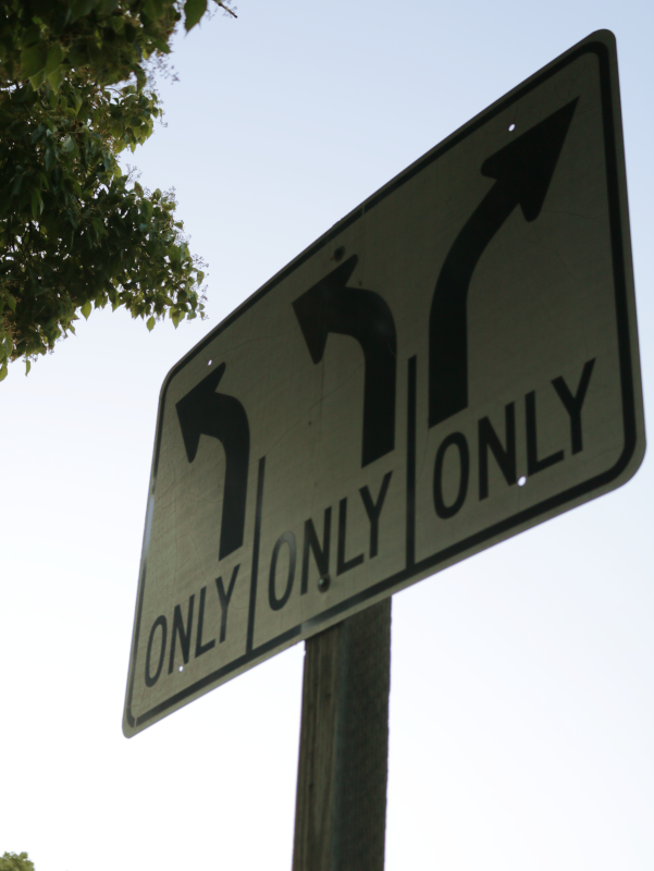 a white street sign, three arrows on the top. the left and middle curving left, the right one being the only one curving right. Each arrow having the words "Only" underneath. 
