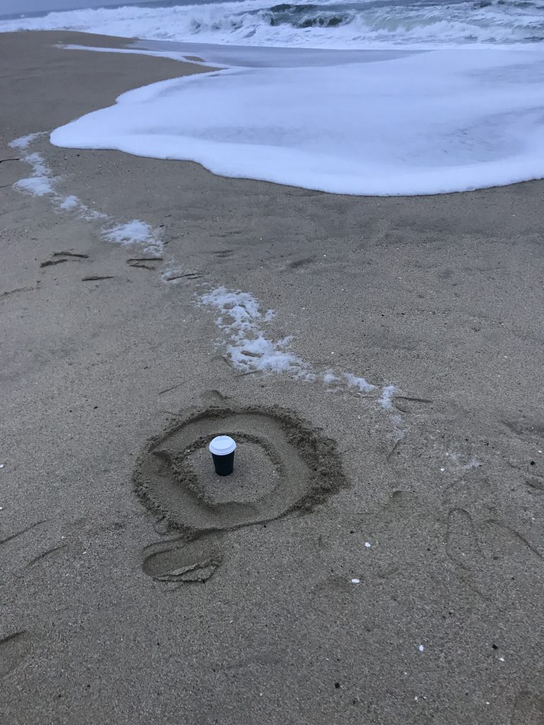 A photo of a coffee cup sitting in the sand at the beach.