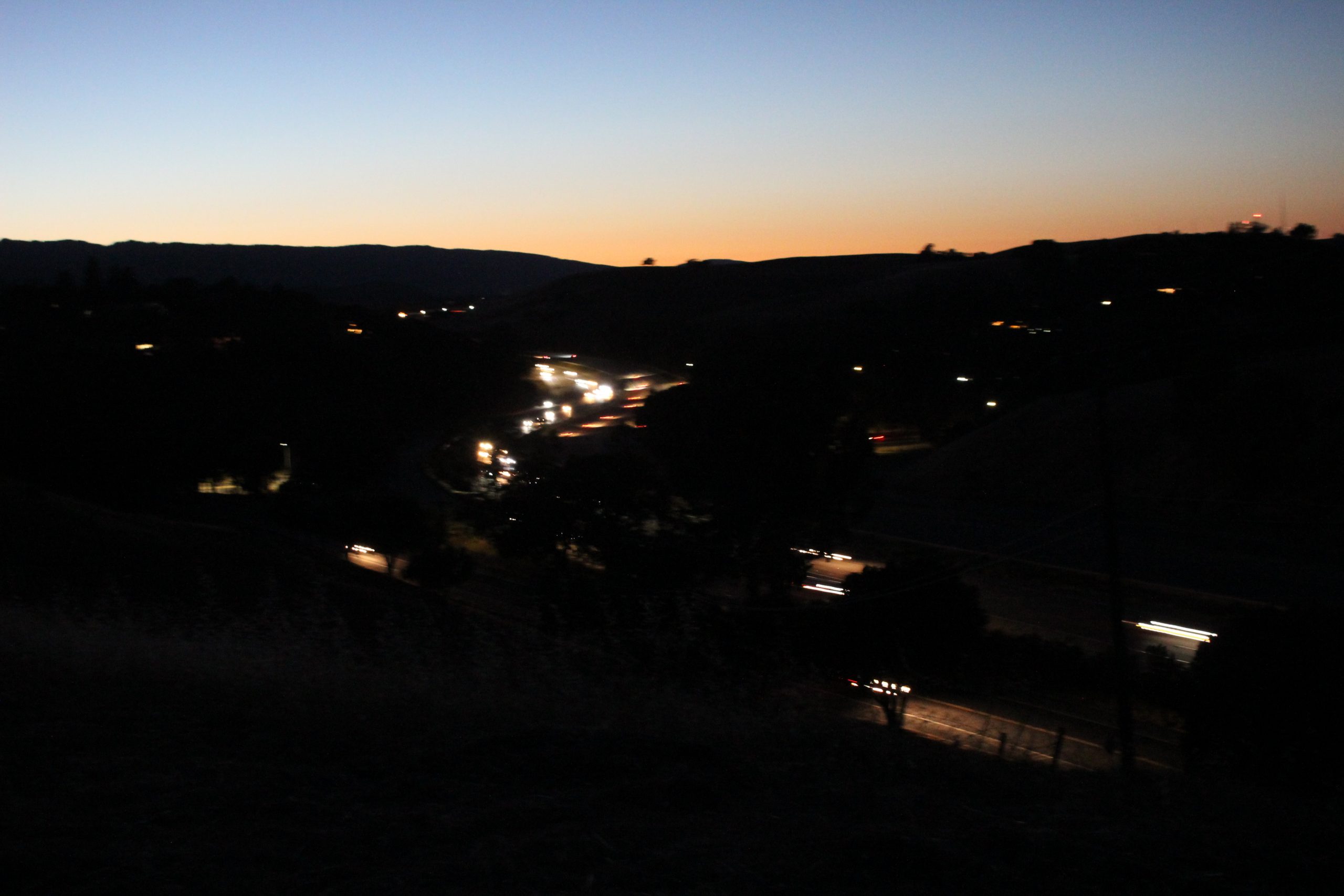 A sunset and a freeway of cars with lights on.