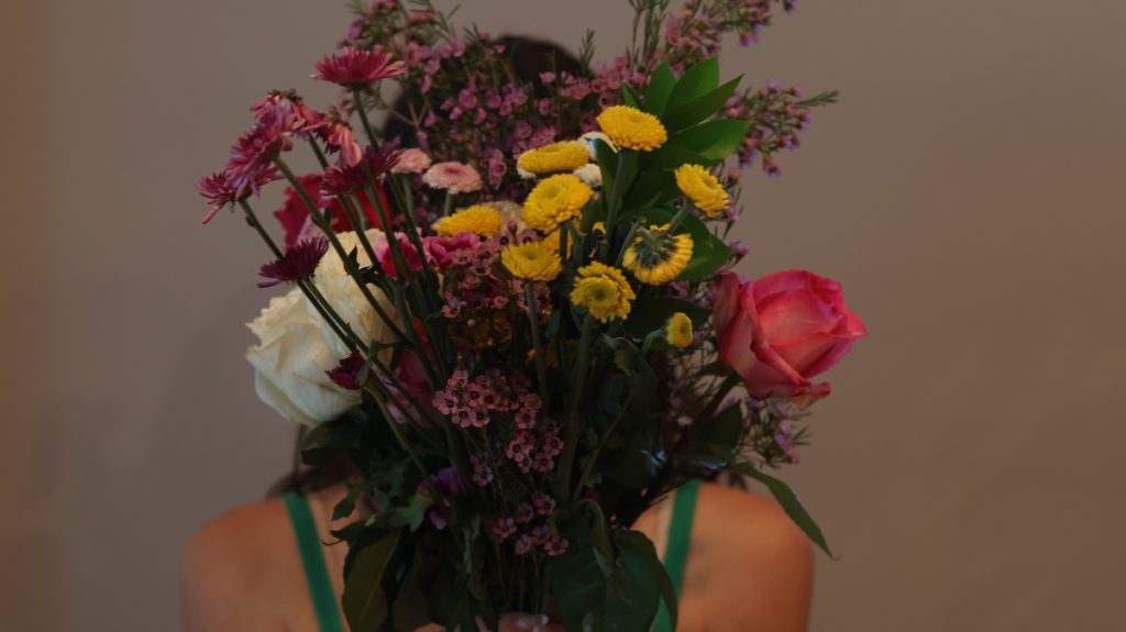 Picture of a girl holding flowers in front of her, blacking the view of her face.