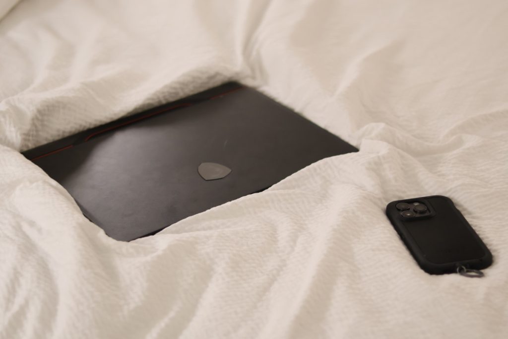 A heavy black computer and a light-weight phone rest on a white blanket.