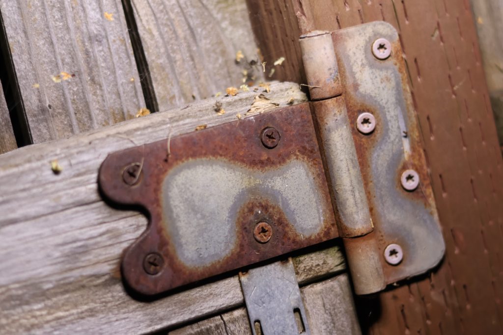 A rusted outdoor gate hinge showing a progression of decay.