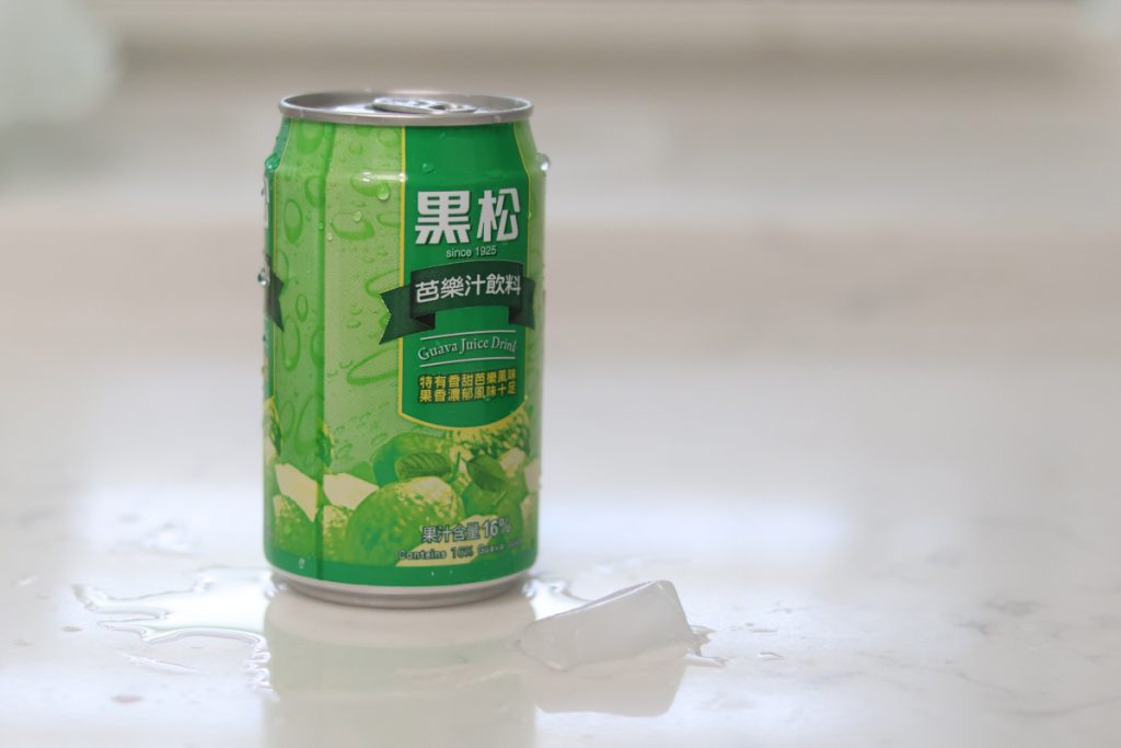Condensation from a green guava juice can creating a puddle on a white countertop with an ice cube in the foreground.
