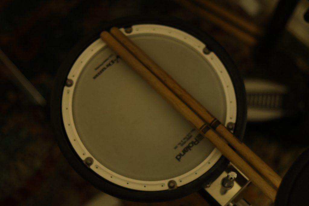 An electronic snare drum with two drumsticks laying on their side