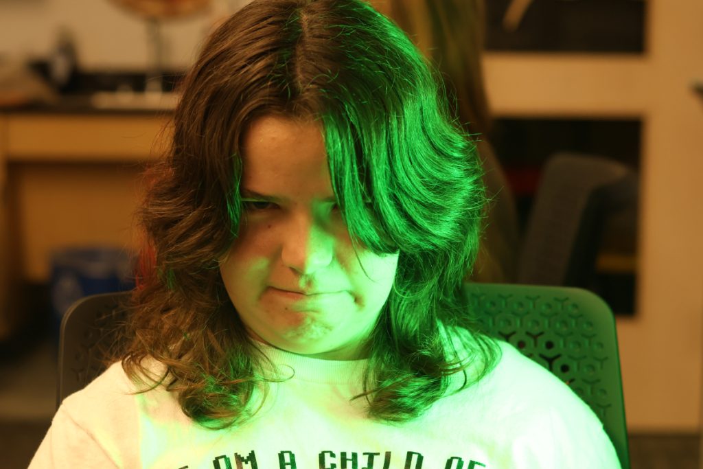 photo of a person making a silly face at the camera, half of his face illuminated by green light