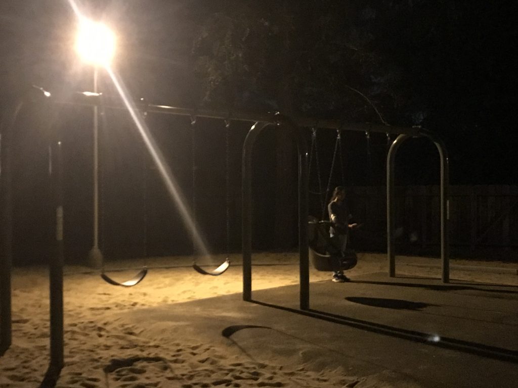 A girl pushing a baby swing in the dark.