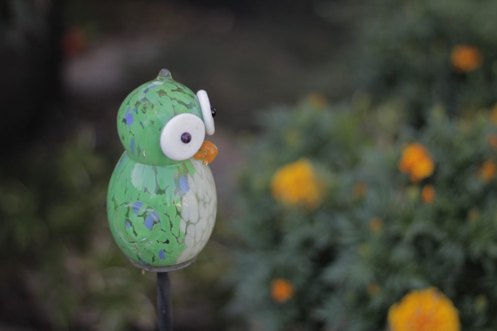 Image of a glass owl with very large eyes. Flowers in the background.