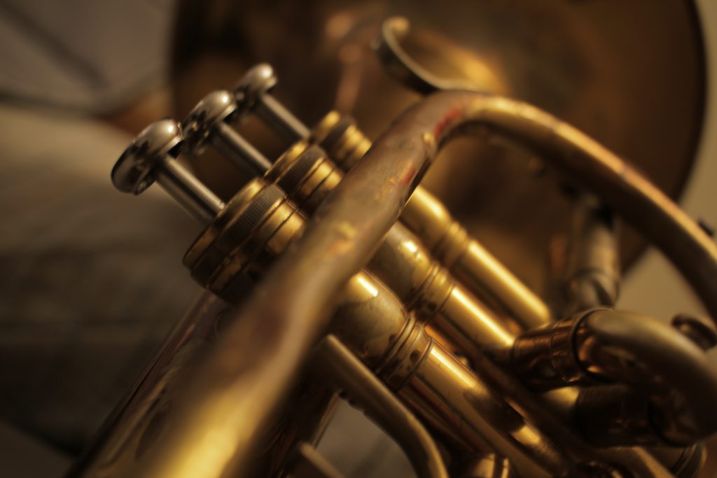 Close up picture of a mellophone for the mouthpiece, with highlights running across the yellow pipework.
